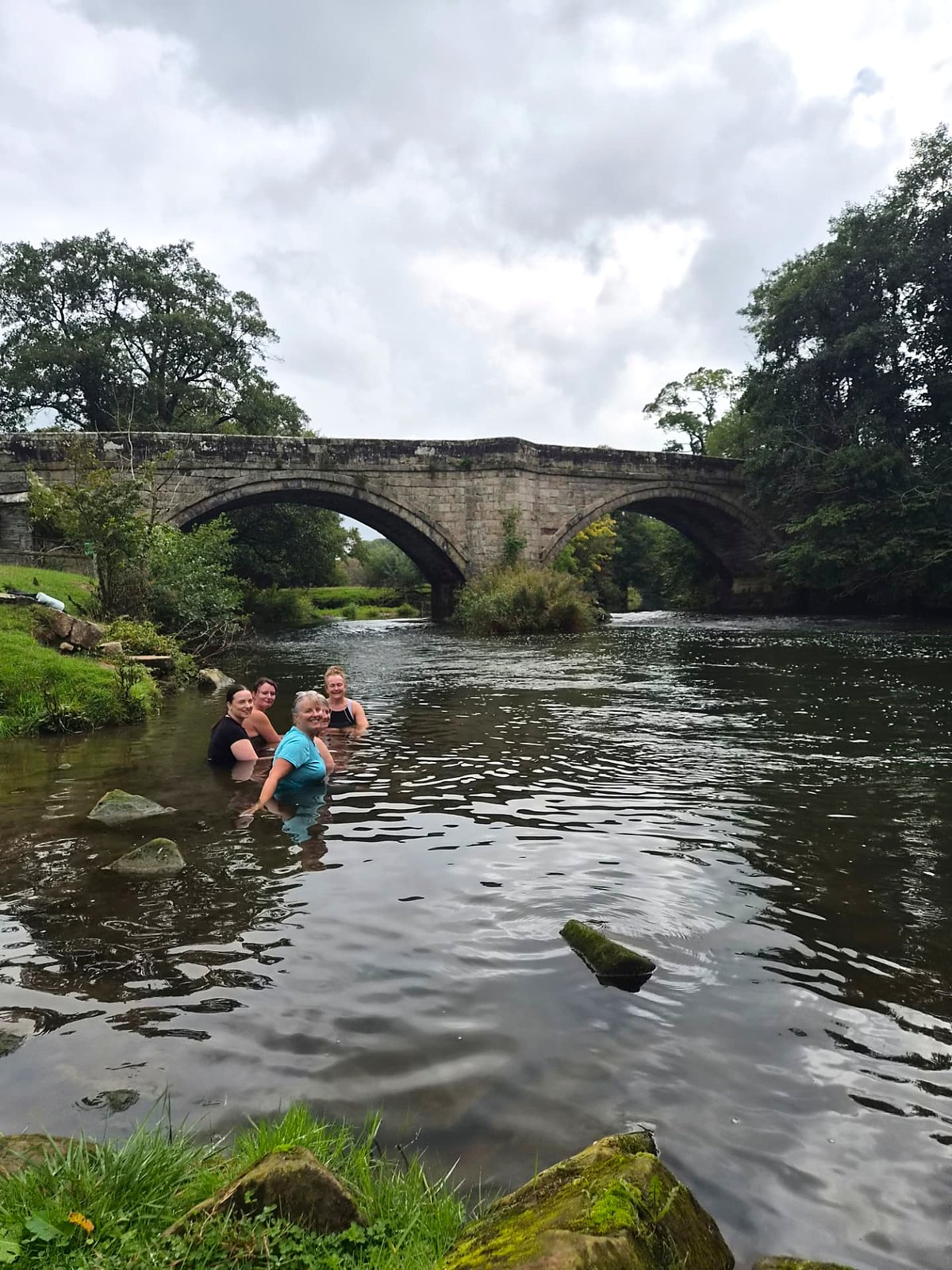 Glow retreat guests sharing a wild swim beneath an old stone bridge