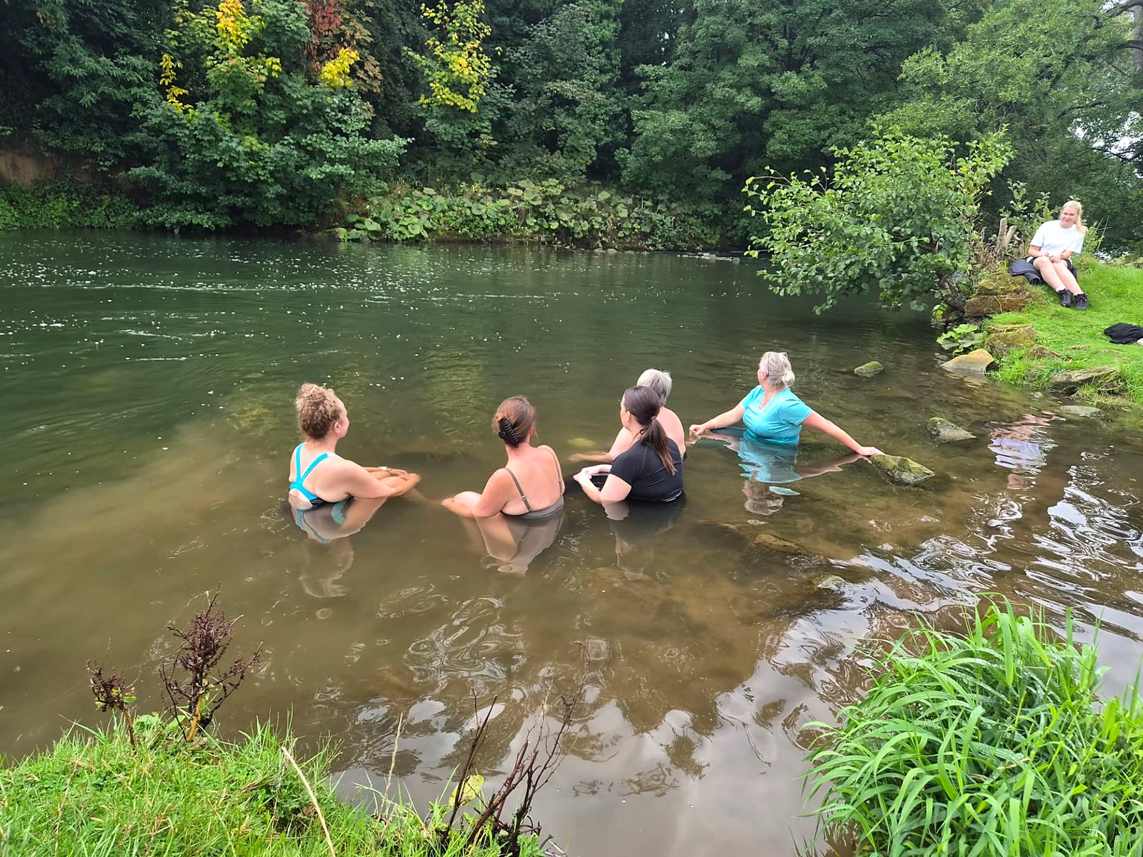 Glow retreat guests sitting together in the shallows of the river