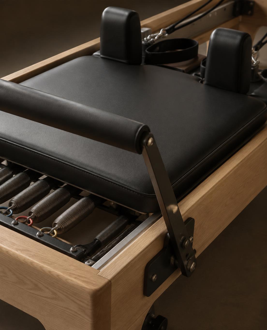 Concept close-up of a black and oak Reformer carriage and springs; not the Glow Up Hub equipment